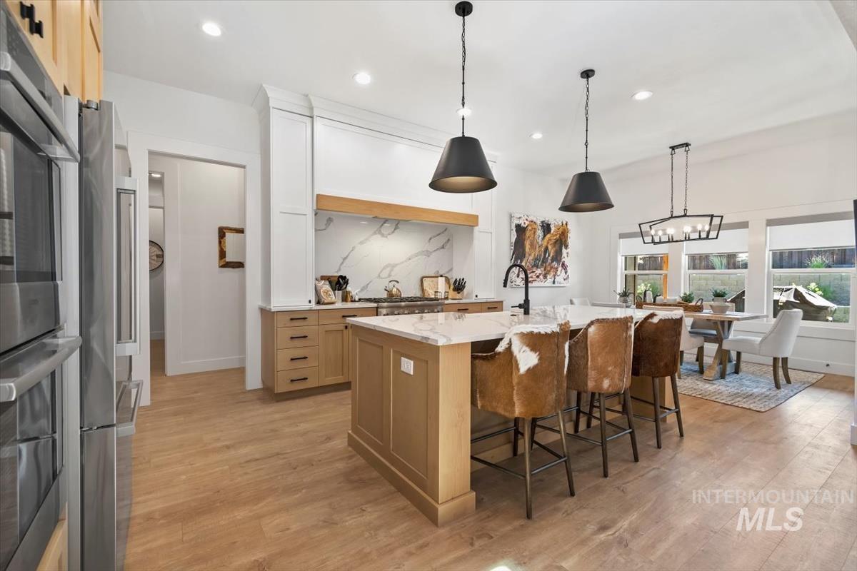 Kitchen featuring decorative light fixtures, light wood finished floors, light brown cabinetry, recessed lighting, and a center island with sink