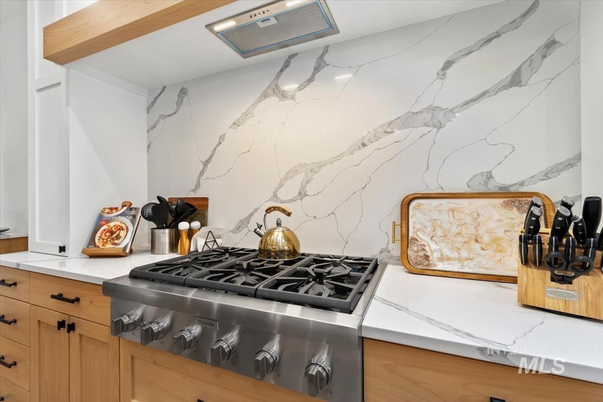 Kitchen with stainless steel gas cooktop, extractor fan, light stone countertops, and light brown cabinetry