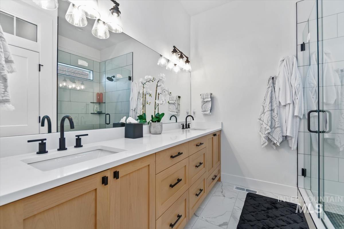 Full bath with a stall shower, double vanity, and light marble finish flooring