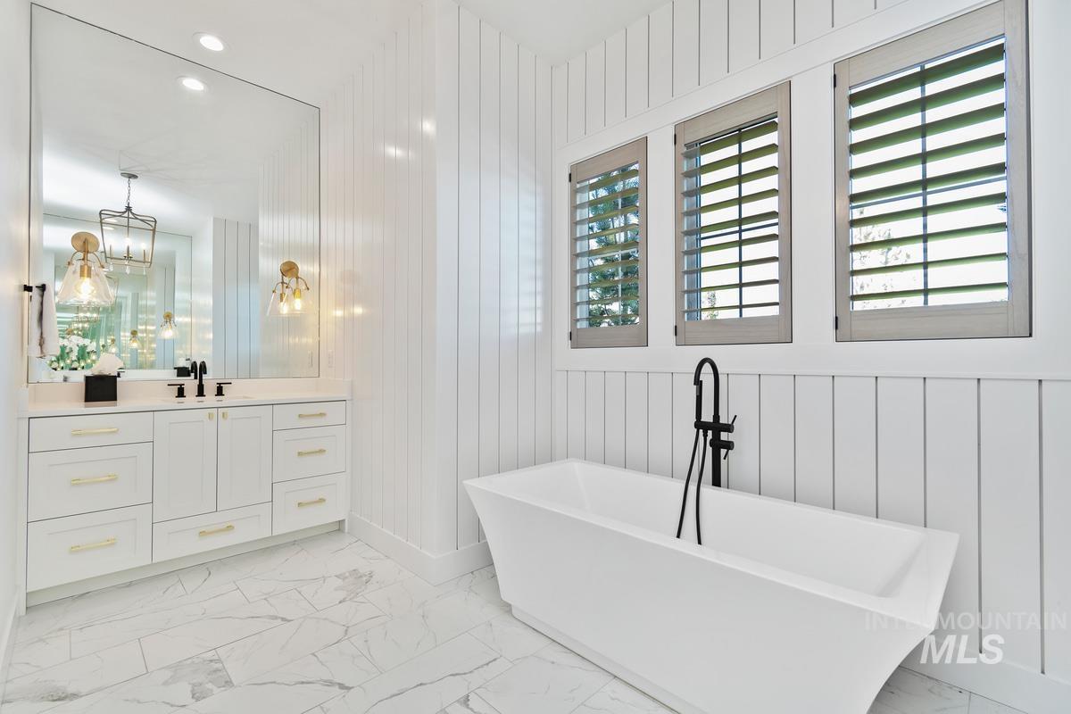 Bathroom featuring light marble finish flooring, vanity, a freestanding tub, recessed lighting, and wood walls