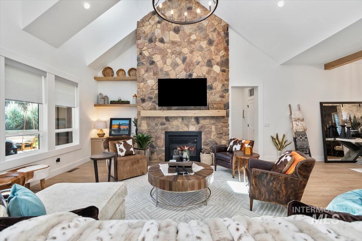Living room featuring wood finished floors, a stone fireplace, high vaulted ceiling, and a chandelier
