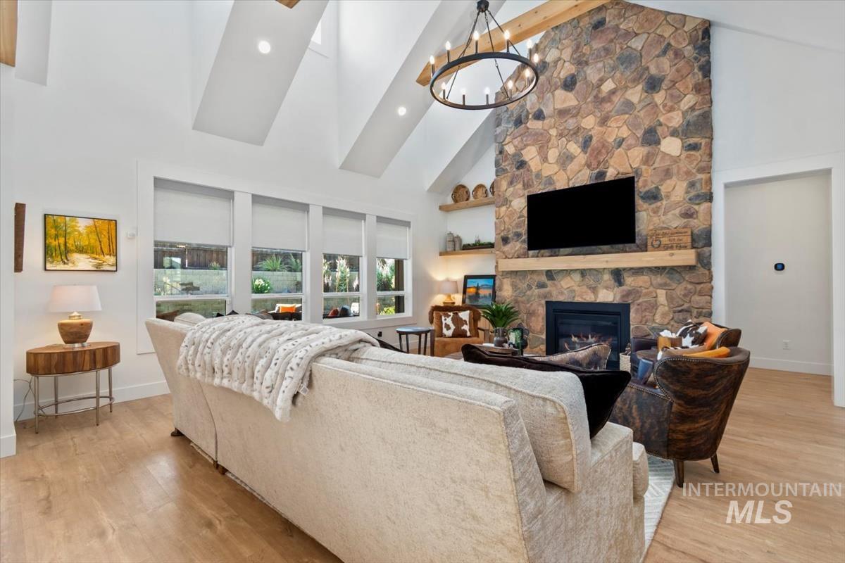 Living room with high vaulted ceiling, a stone fireplace, light wood finished floors, a chandelier, and recessed lighting