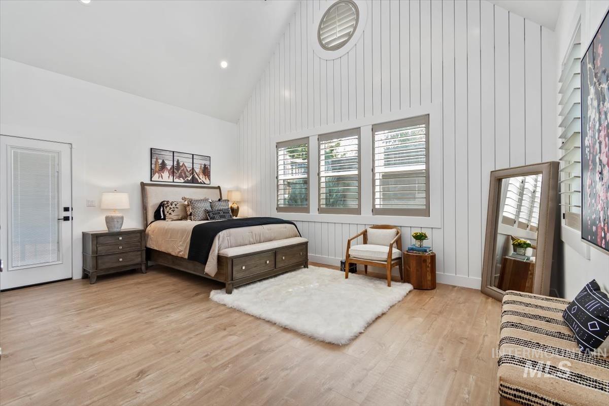 Bedroom with high vaulted ceiling, light wood-style floors, recessed lighting, and wooden walls