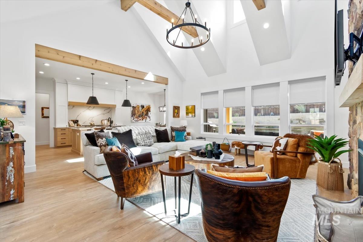 Living area with high vaulted ceiling, light wood finished floors, a chandelier, beamed ceiling, and a fireplace