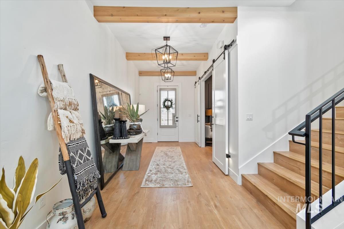 Foyer entrance featuring a barn door, beam ceiling, light wood-style flooring, and a chandelier