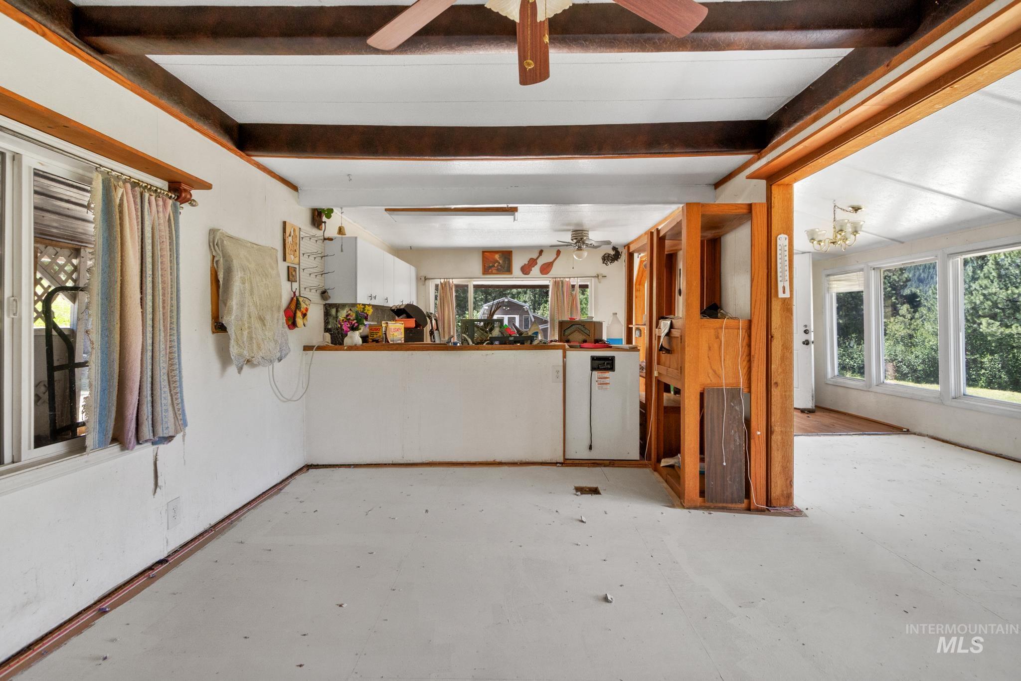 Open-concept living space featuring exposed wood ceiling beams, a ceiling fan, and a pass-through counter to the kitchen area