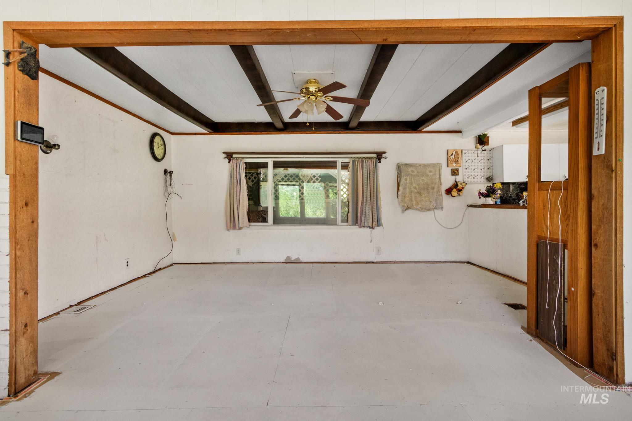 Spacious interior room featuring exposed wood ceiling beams, a ceiling fan, and a double window