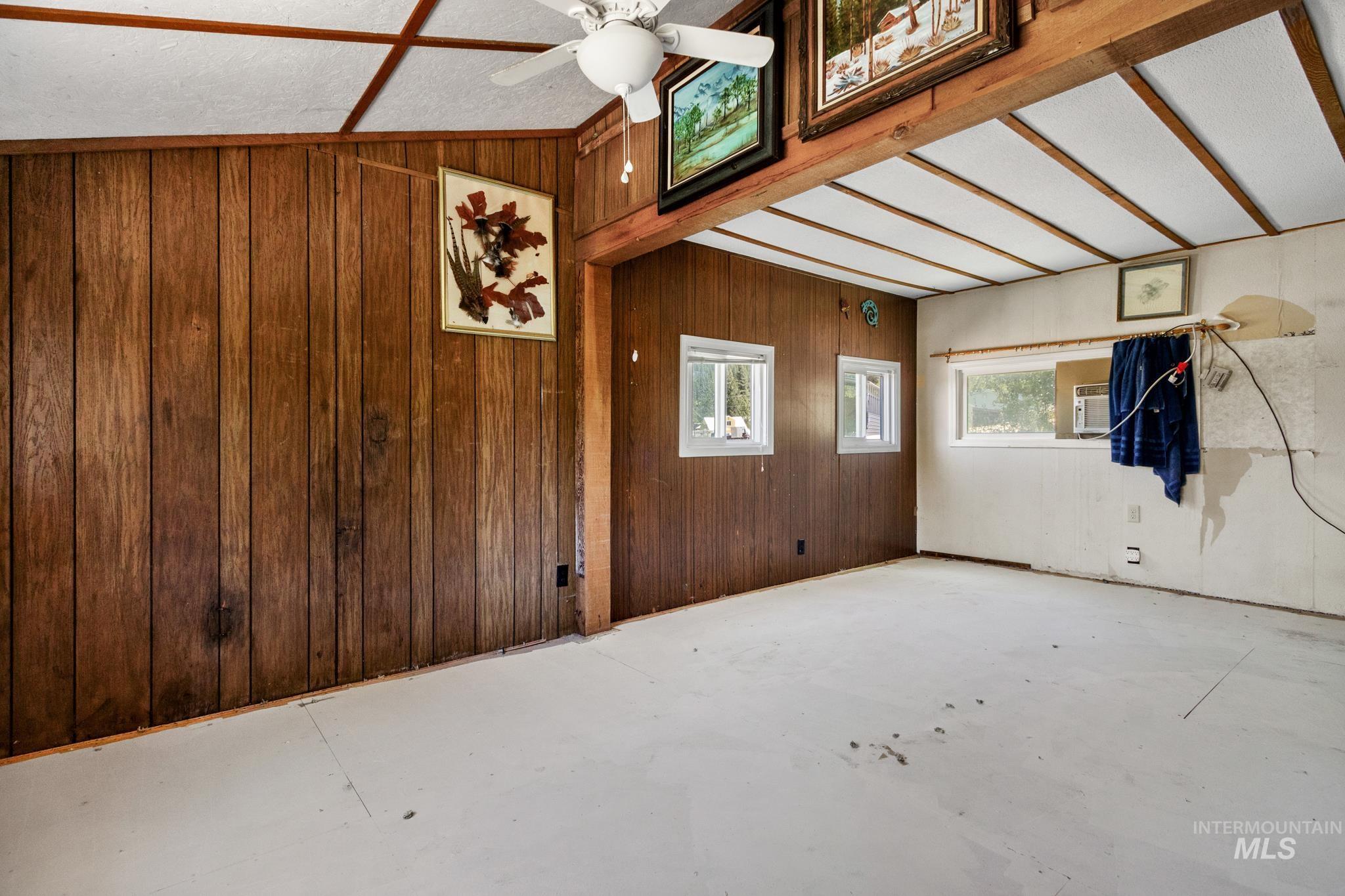 Interior space featuring wood paneling, wood-finish ceiling beams, a ceiling fan, and multiple windows