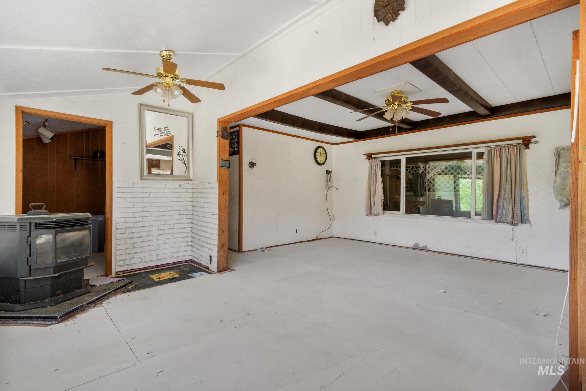 Interior space featuring exposed wood beams, a large window, two ceiling fans, painted white brick accents, and a built-in stove unit