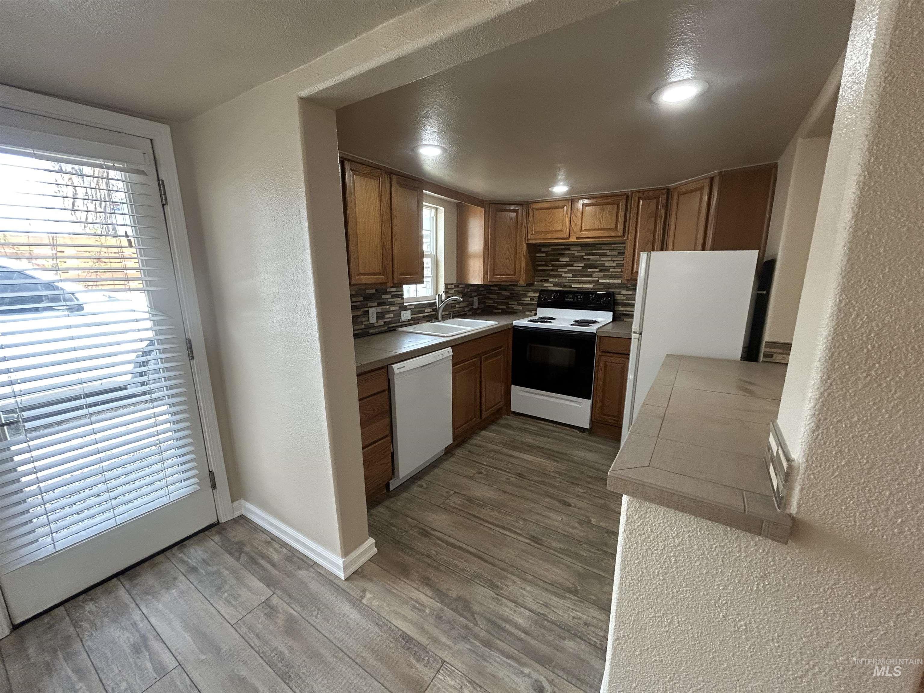 Kitchen featuring wood-finish flooring, wood cabinetry, a tiled backsplash, recessed lighting, and a white appliance suite
