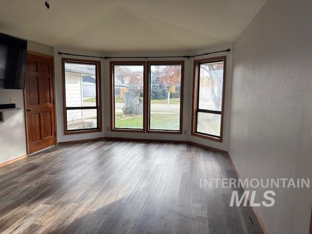 Empty room featuring wood finished floors, plenty of natural light, and vaulted ceiling