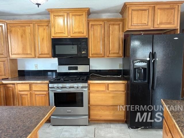 Kitchen with black appliances, dark countertops, brown cabinets, and light tile patterned floors