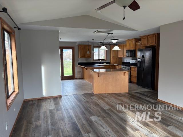 Kitchen with brown cabinetry, dark countertops, black appliances, a breakfast bar, and lofted ceiling