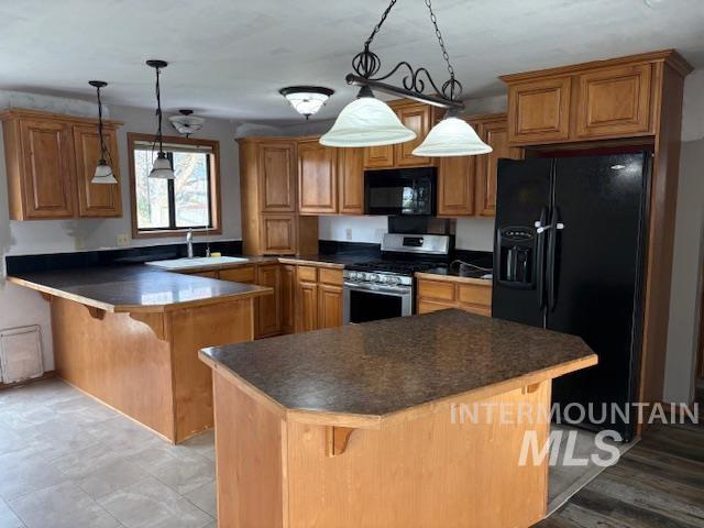 Kitchen with a kitchen breakfast bar, brown cabinets, dark countertops, black appliances, and hanging light fixtures