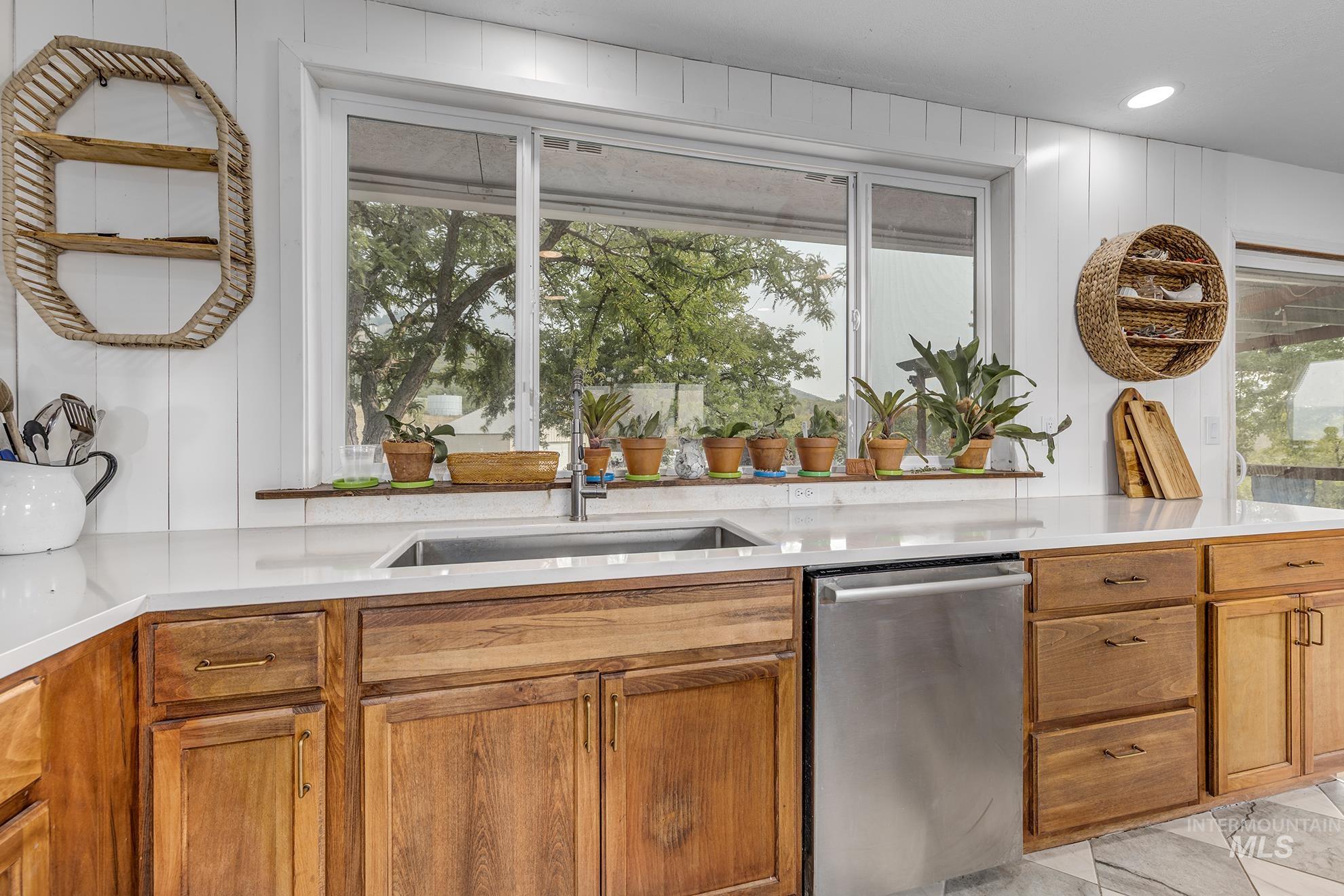 Kitchen featuring stainless steel dishwasher, brown cabinets, and light stone counters