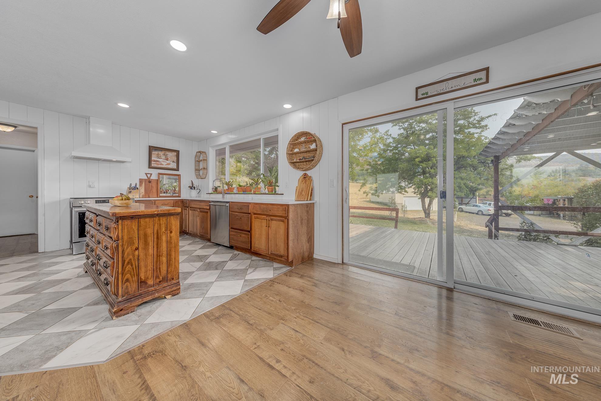 Kitchen with brown cabinets, wall chimney exhaust hood, recessed lighting, light wood-style floors, and appliances with stainless steel finishes