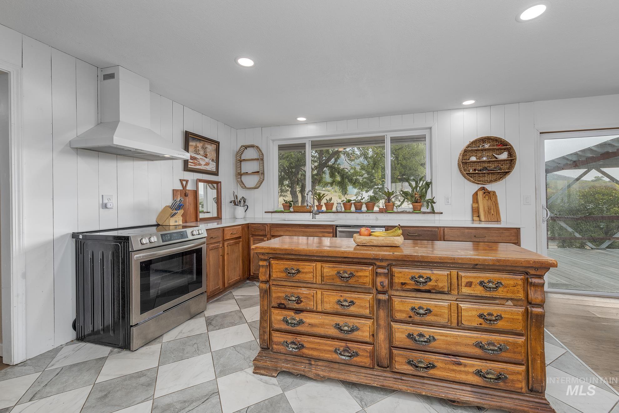 Kitchen with stainless steel electric range, wall chimney range hood, brown cabinets, recessed lighting, and a kitchen island