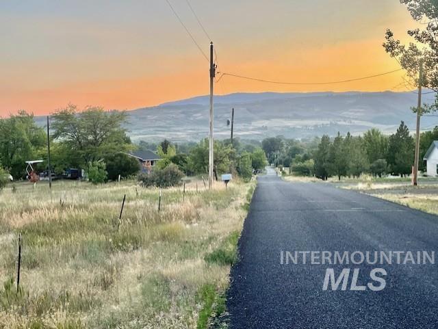 View of asphalt street featuring view of wooded area and a mountain view