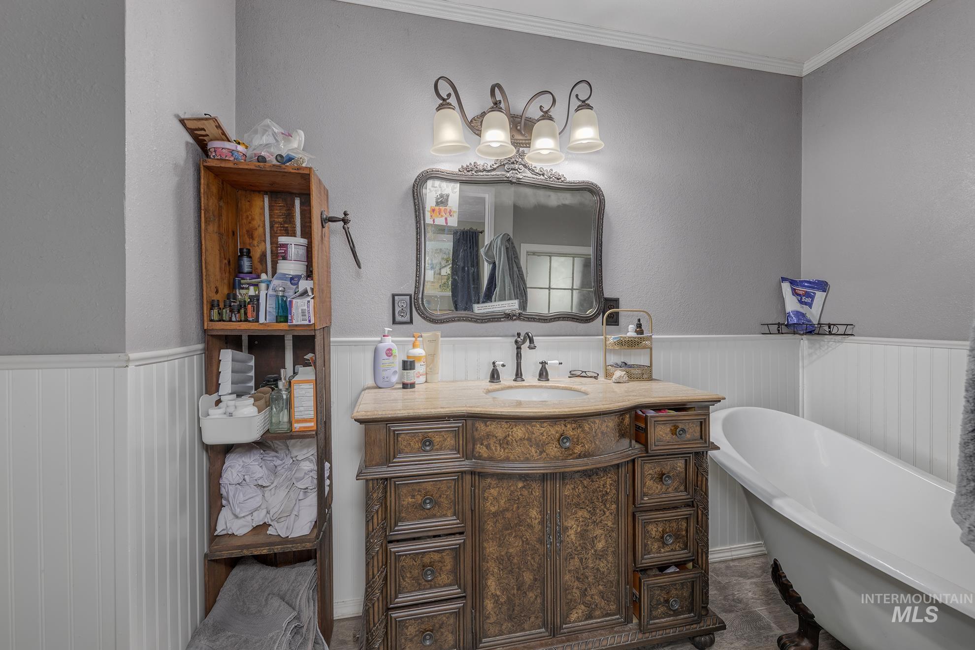 Full bath with a freestanding tub, vanity, a wainscoted wall, and ornamental molding