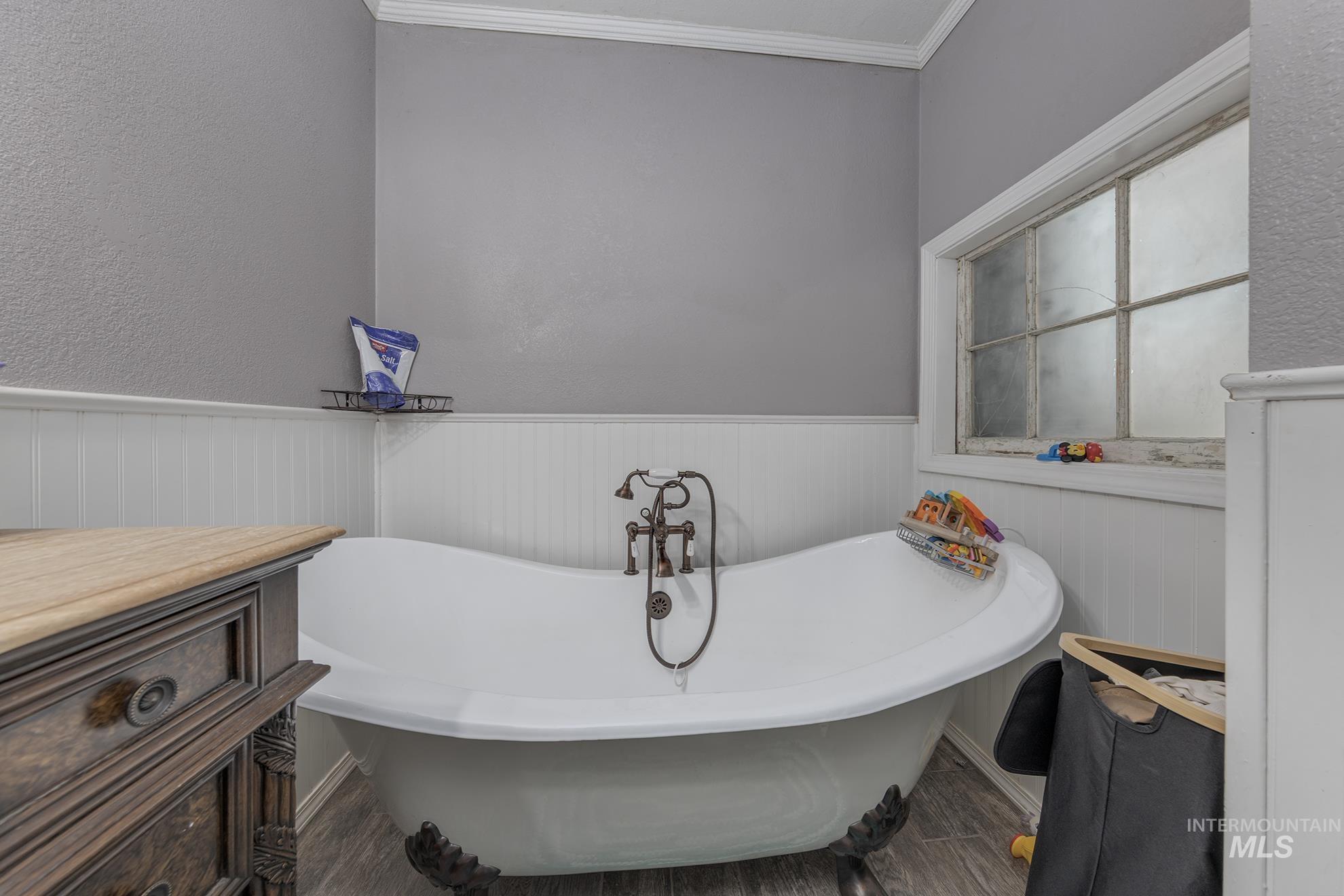 Bathroom featuring a soaking tub, wood finished floors, ornamental molding, wainscoting, and a textured wall