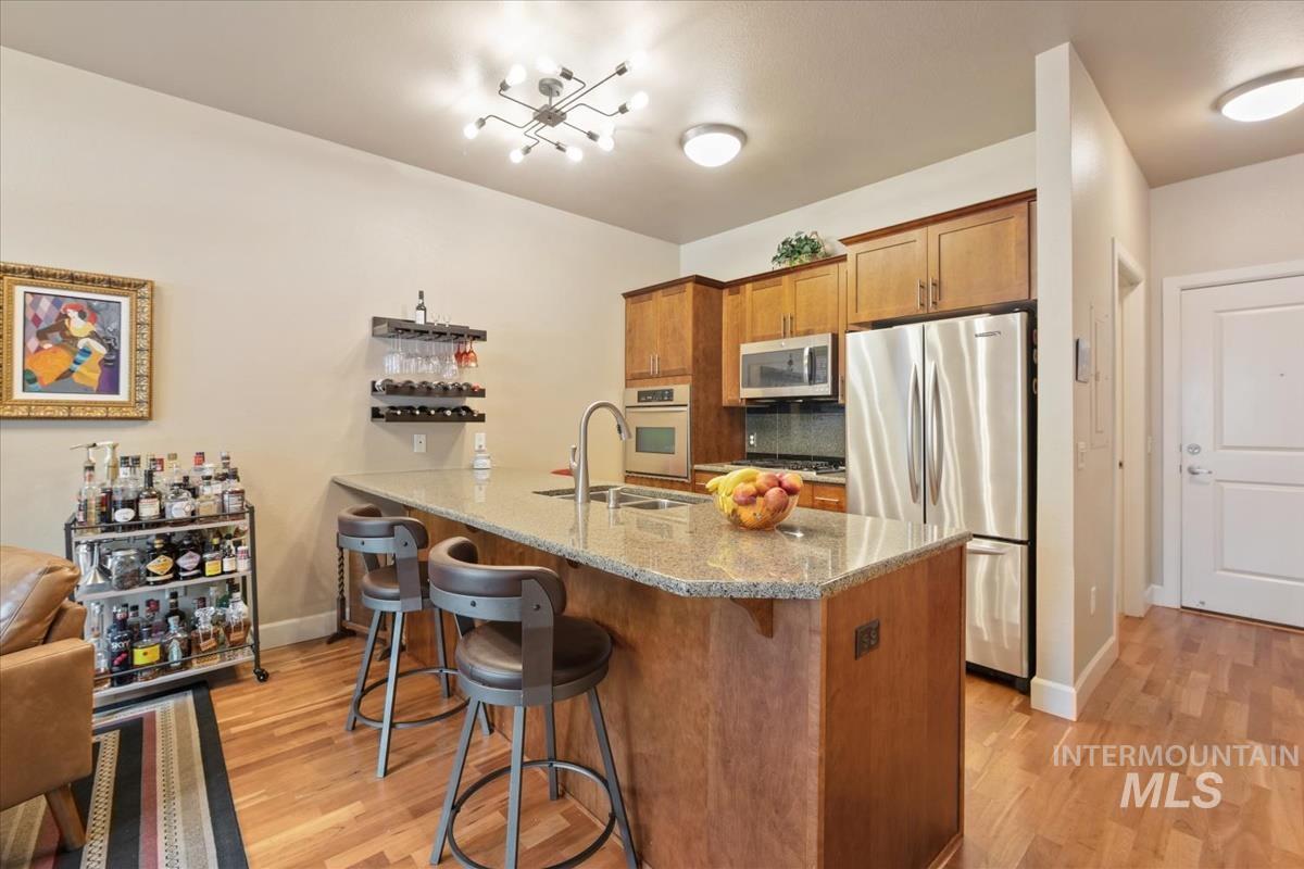 Kitchen with wood finish cabinetry, stainless steel appliances, light stone counters, a kitchen breakfast bar, and light wood-style floors