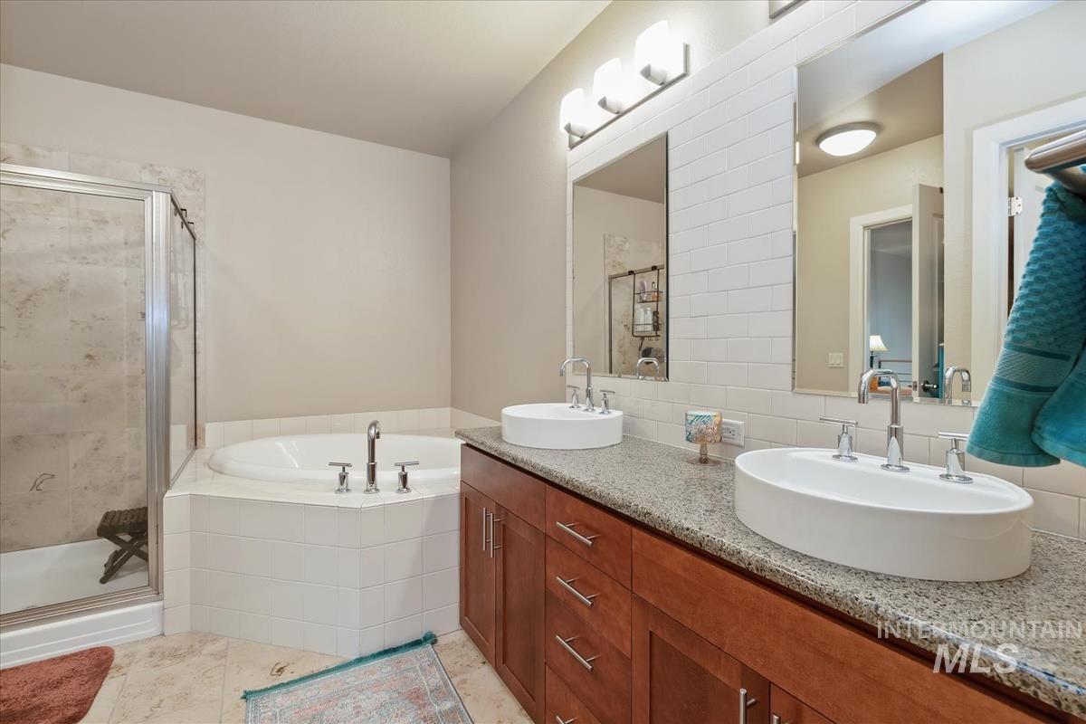 Full bathroom featuring double vanity, a shower stall, a garden tub, and tasteful backsplash