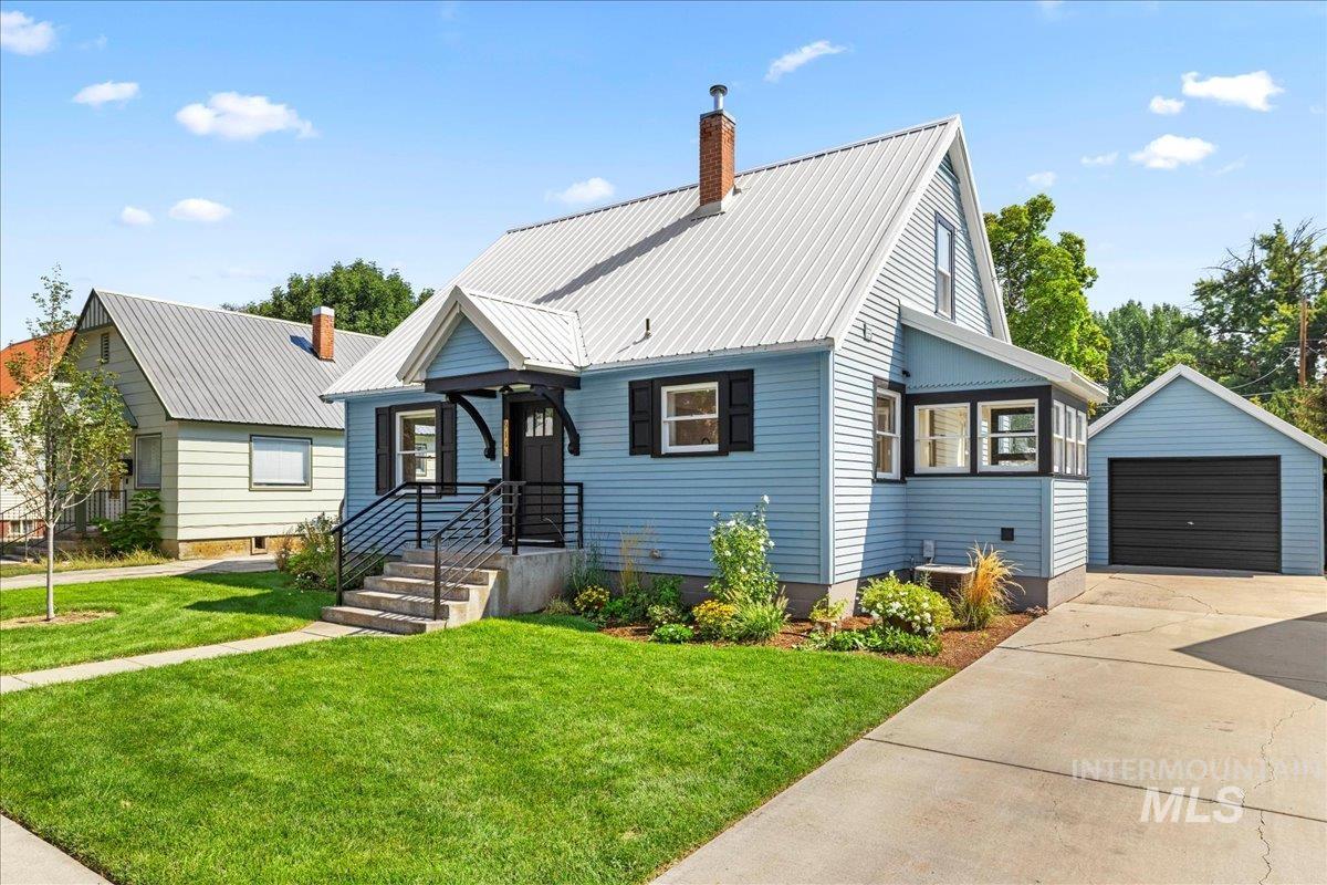 View of front of house with a garage, an outbuilding, a front yard, and a metal roof