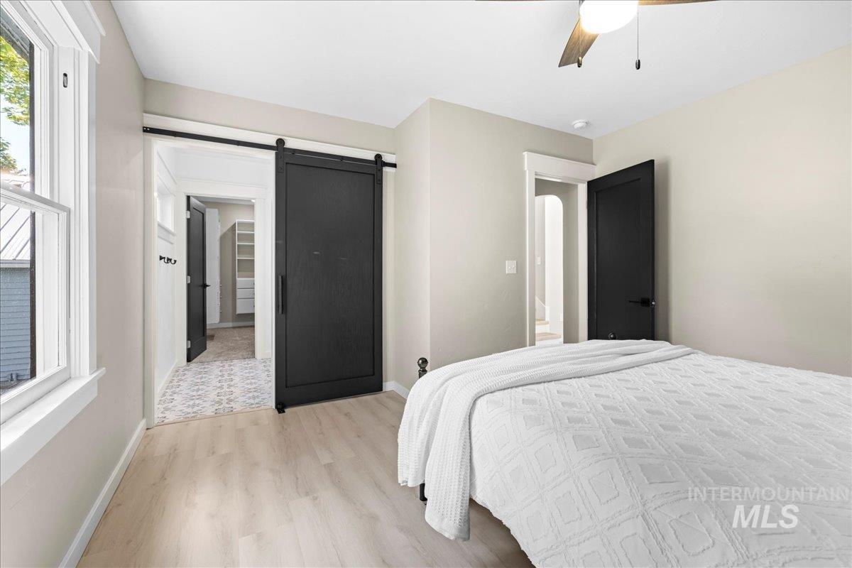Bedroom with light wood-type flooring, a barn door, a spacious closet, and a ceiling fan