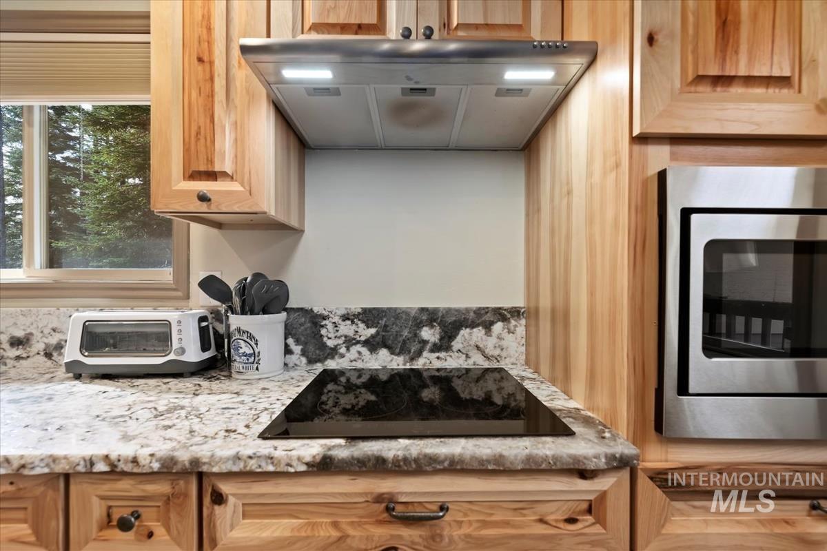 Kitchen with light stone counters, stainless steel microwave, extractor fan, and black electric stovetop