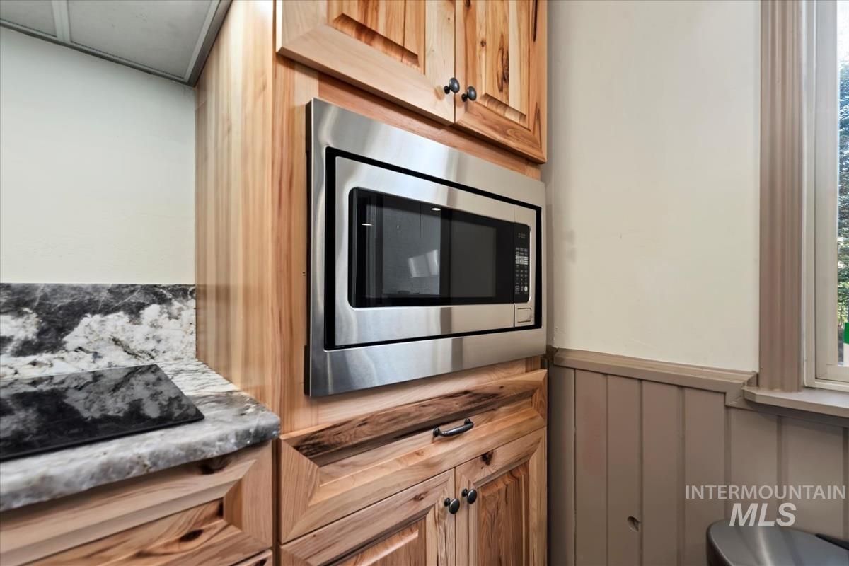 Kitchen featuring stainless steel microwave, wainscoting, brown cabinetry, and black electric stovetop