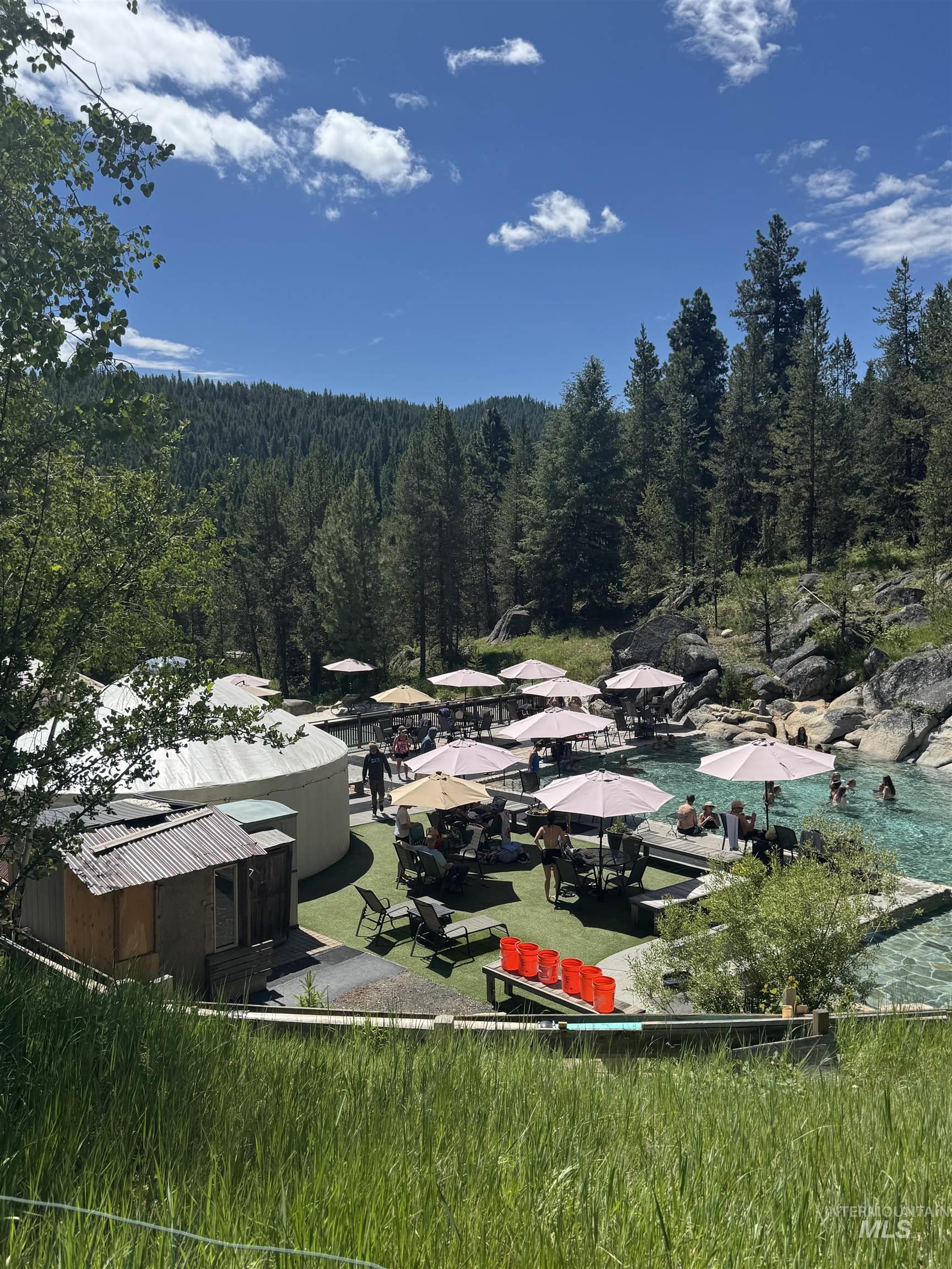 Outdoor recreational area featuring multiple pools, shaded seating, and a forested backdrop