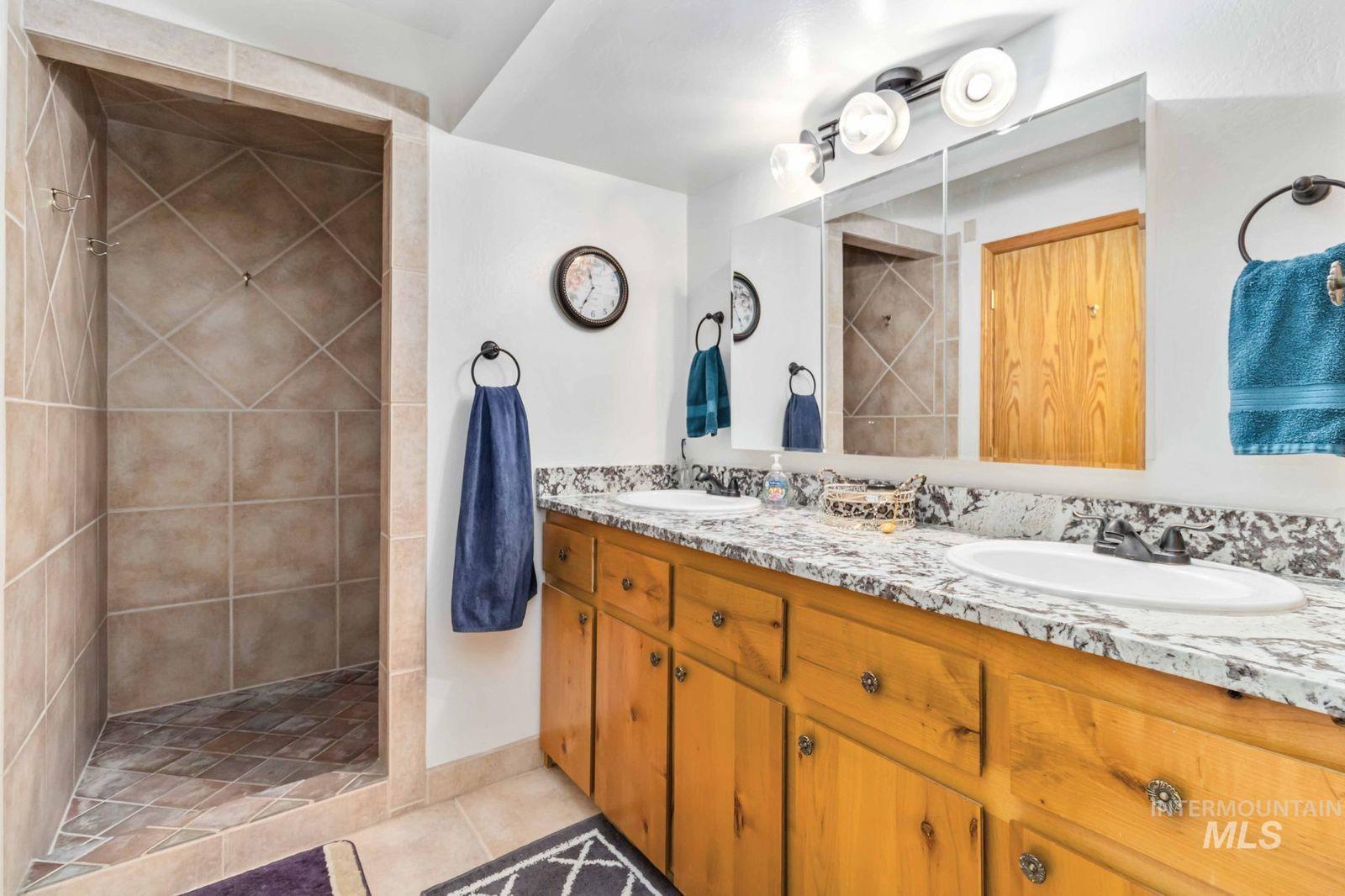 Bathroom with light tile patterned floors, double vanity, and walk in shower