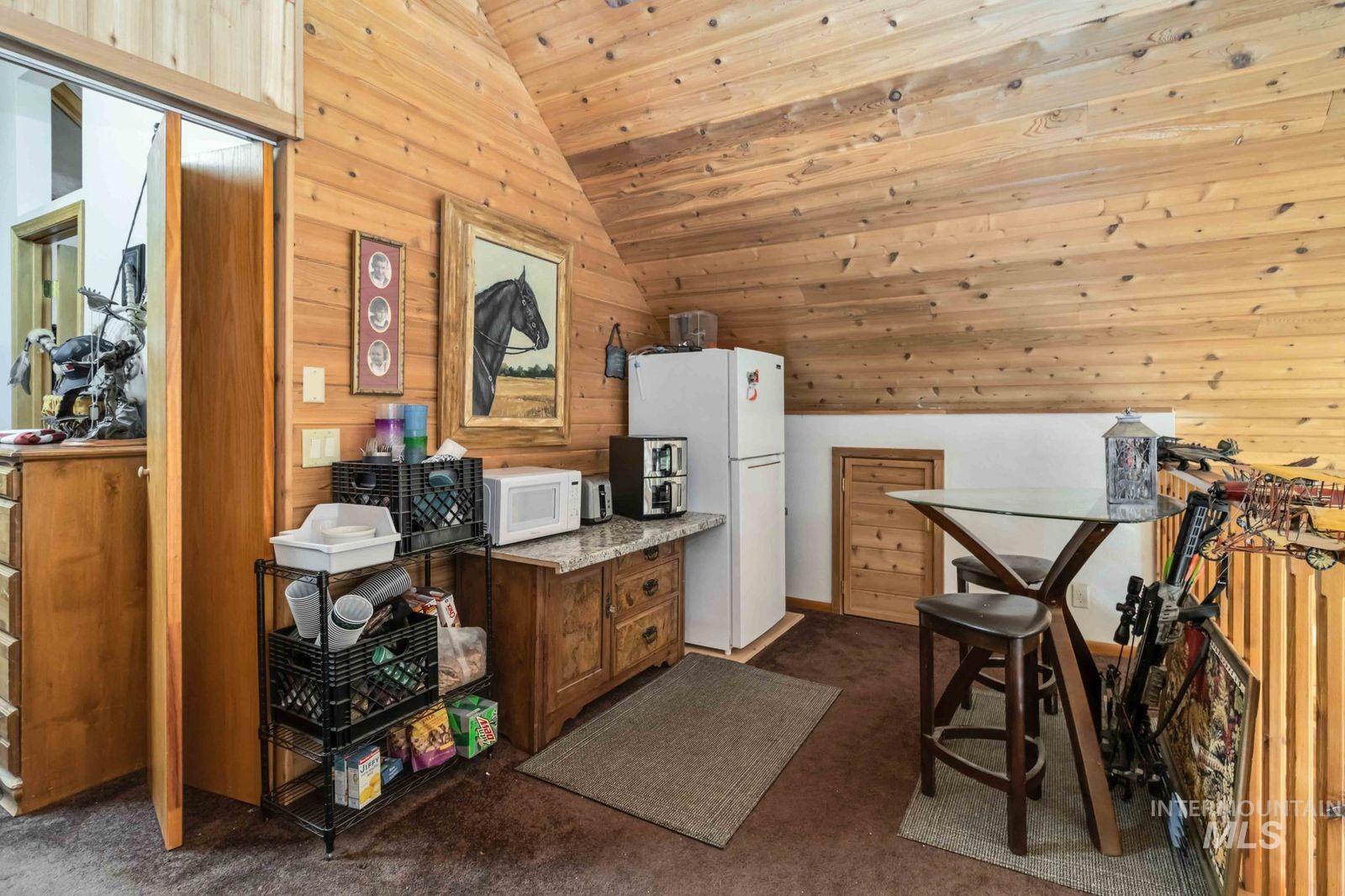 Kitchen with wood walls, vaulted ceiling, white appliances, dark colored carpet, and wood ceiling