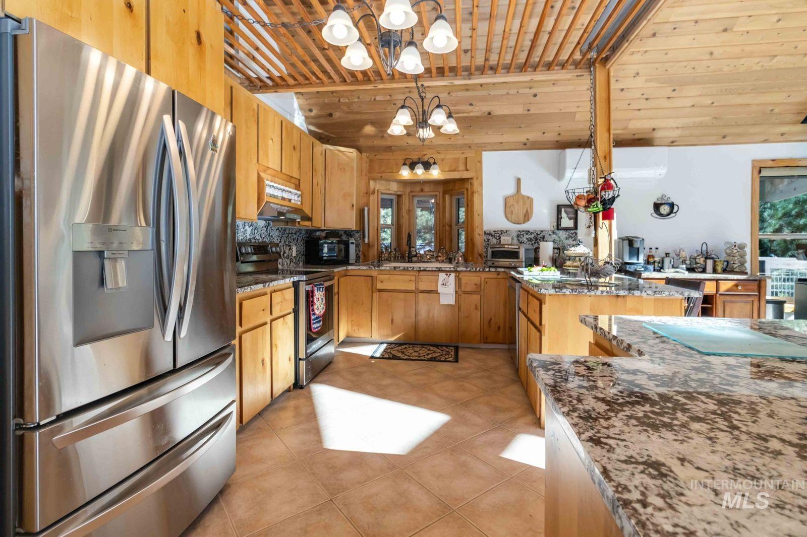 Kitchen with appliances with stainless steel finishes, hanging light fixtures, dark stone countertops, backsplash, and light tile patterned floors