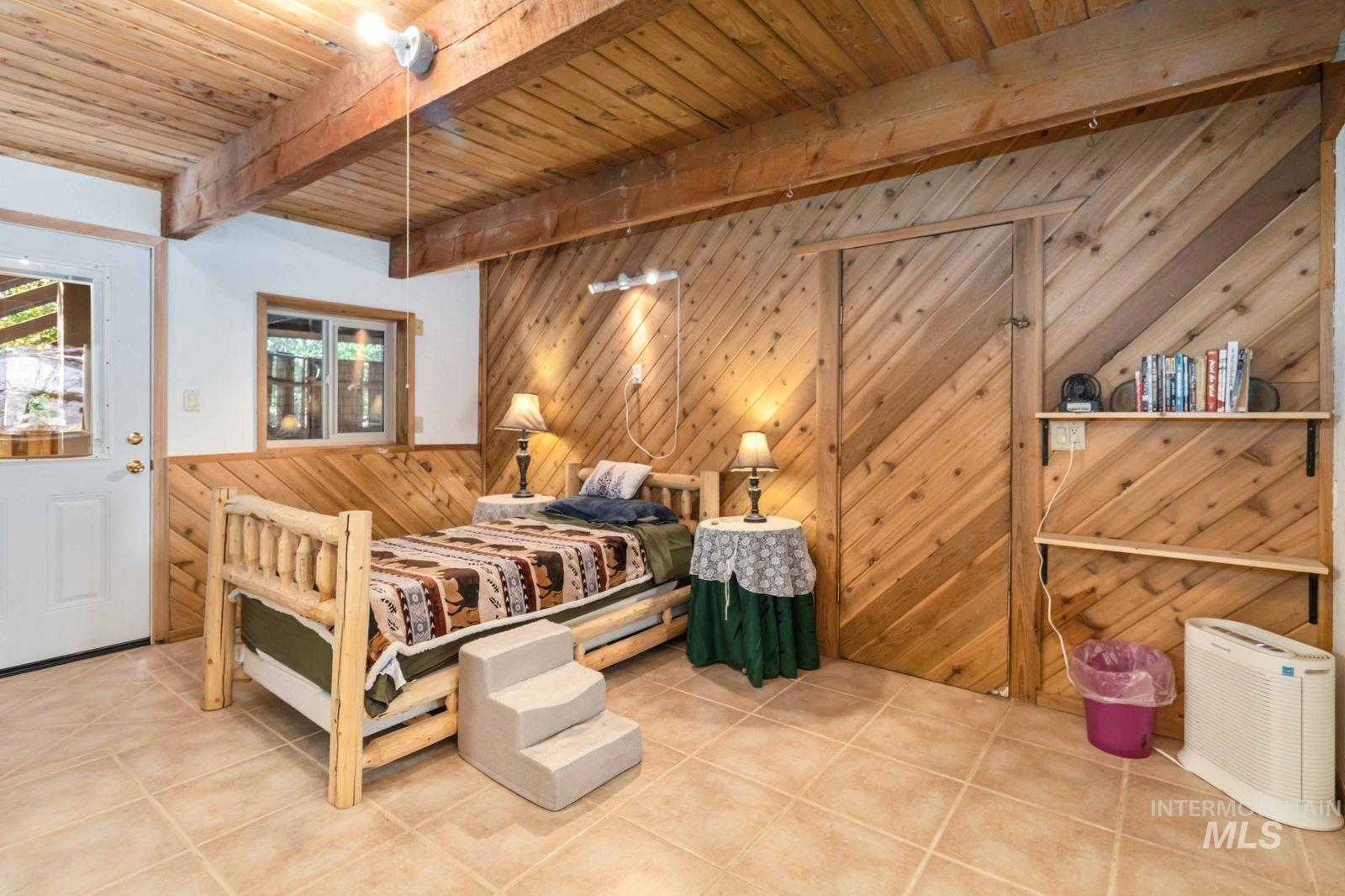 Bedroom with wooden walls, tile patterned flooring, a wainscoted wall, and a wooden ceiling with exposed beams