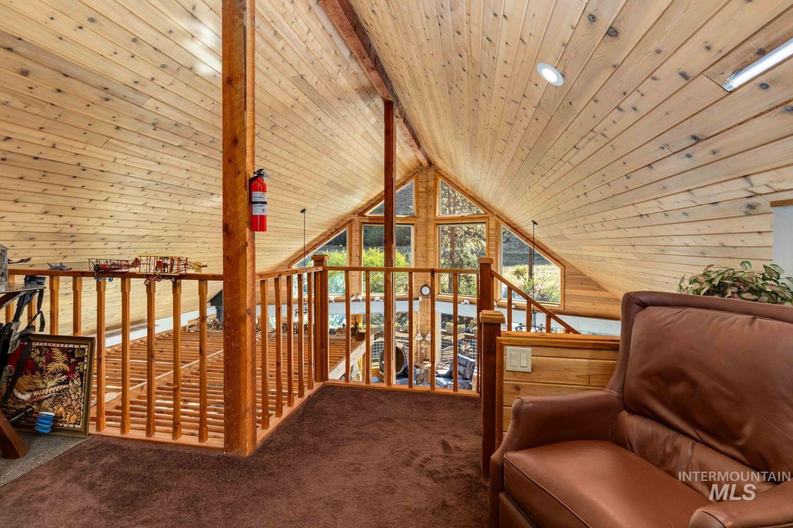 Living area with wood ceiling, carpet flooring, and an upstairs landing