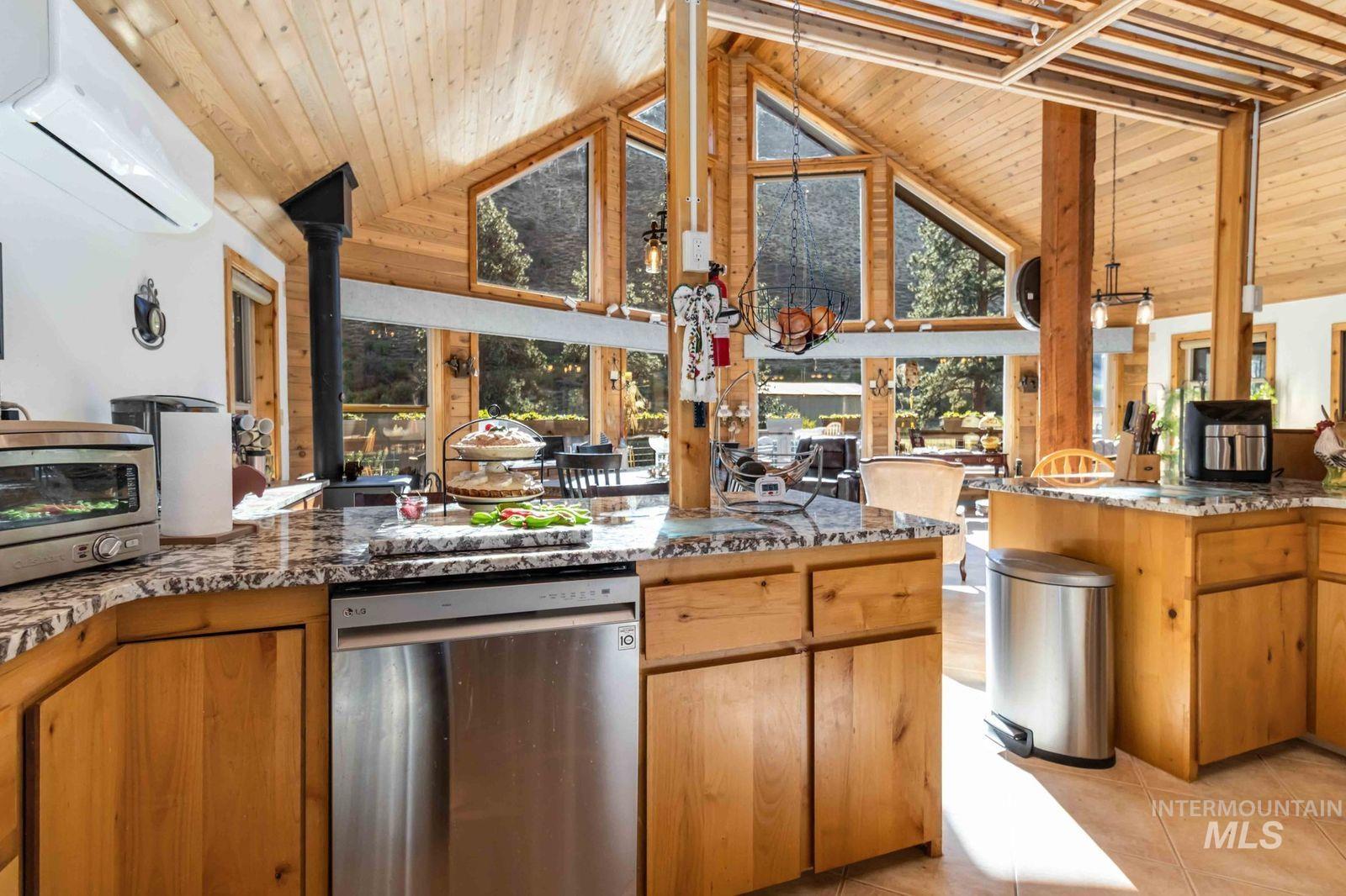 Kitchen with dark stone counters, dishwasher, a wall unit AC, brown cabinetry, and a wood stove