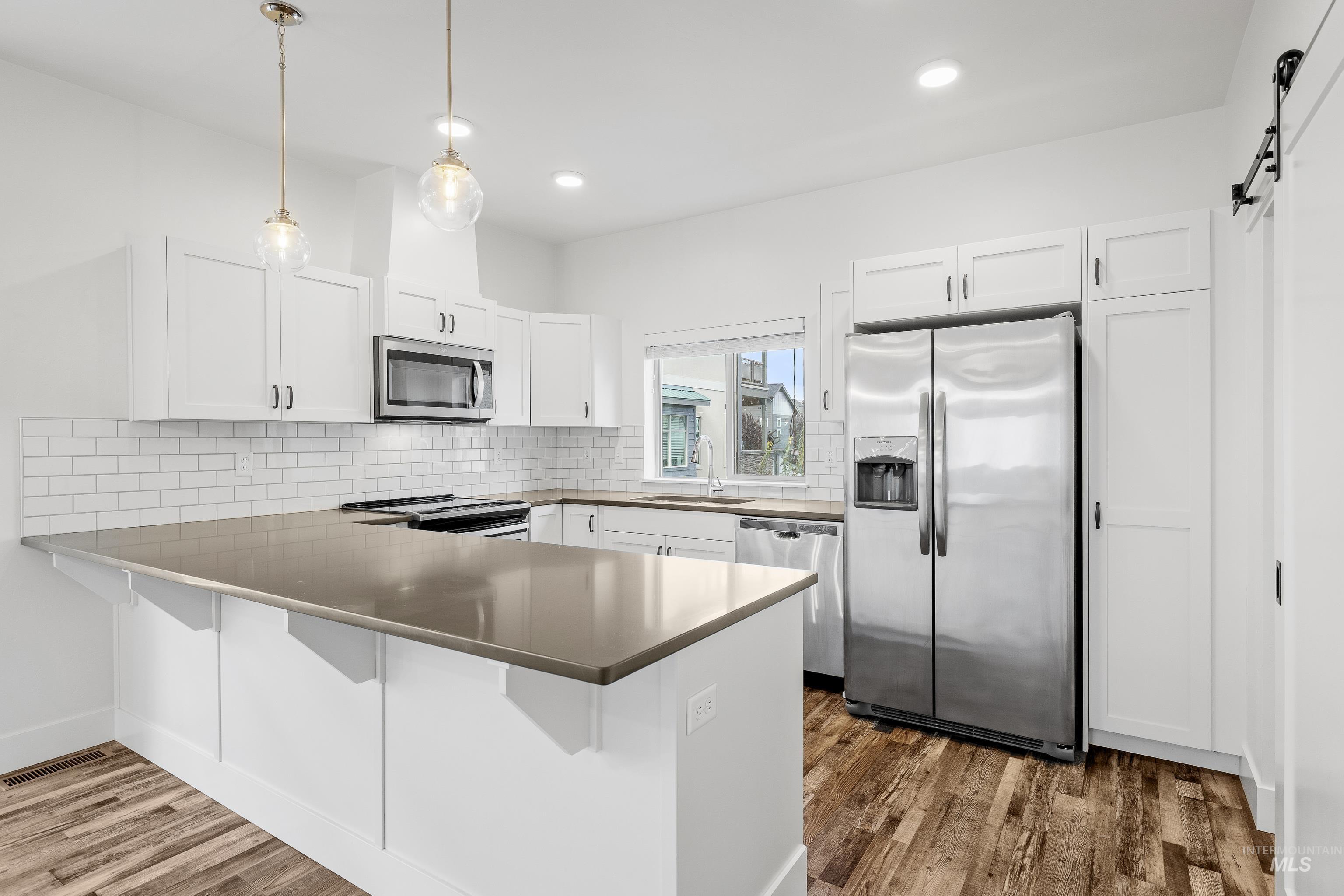Kitchen featuring decorative light fixtures, appliances with stainless steel finishes, white cabinets, a barn door, and recessed lighting