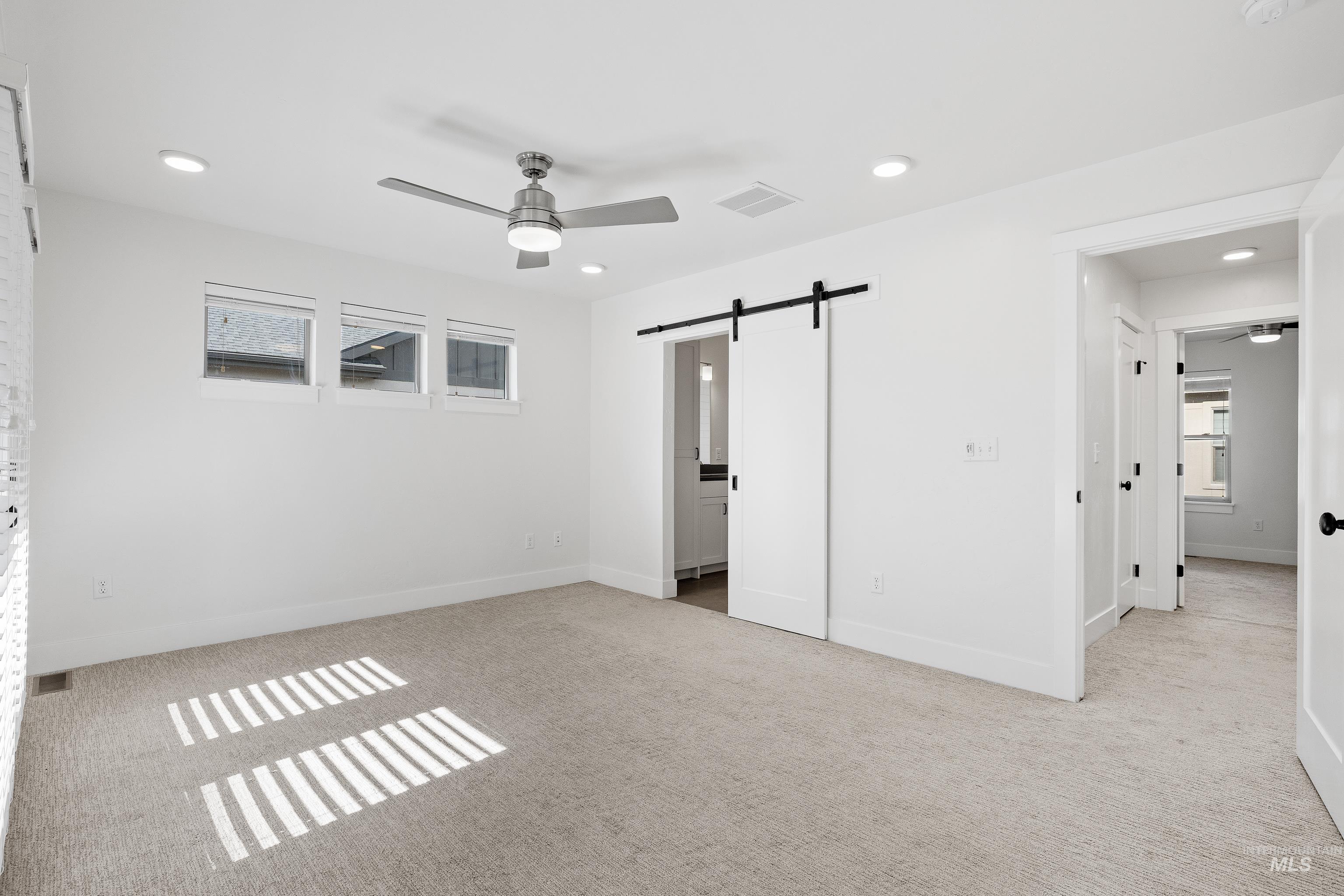 Unfurnished bedroom with a barn door, recessed lighting, light colored carpet, a ceiling fan, and ensuite bathroom