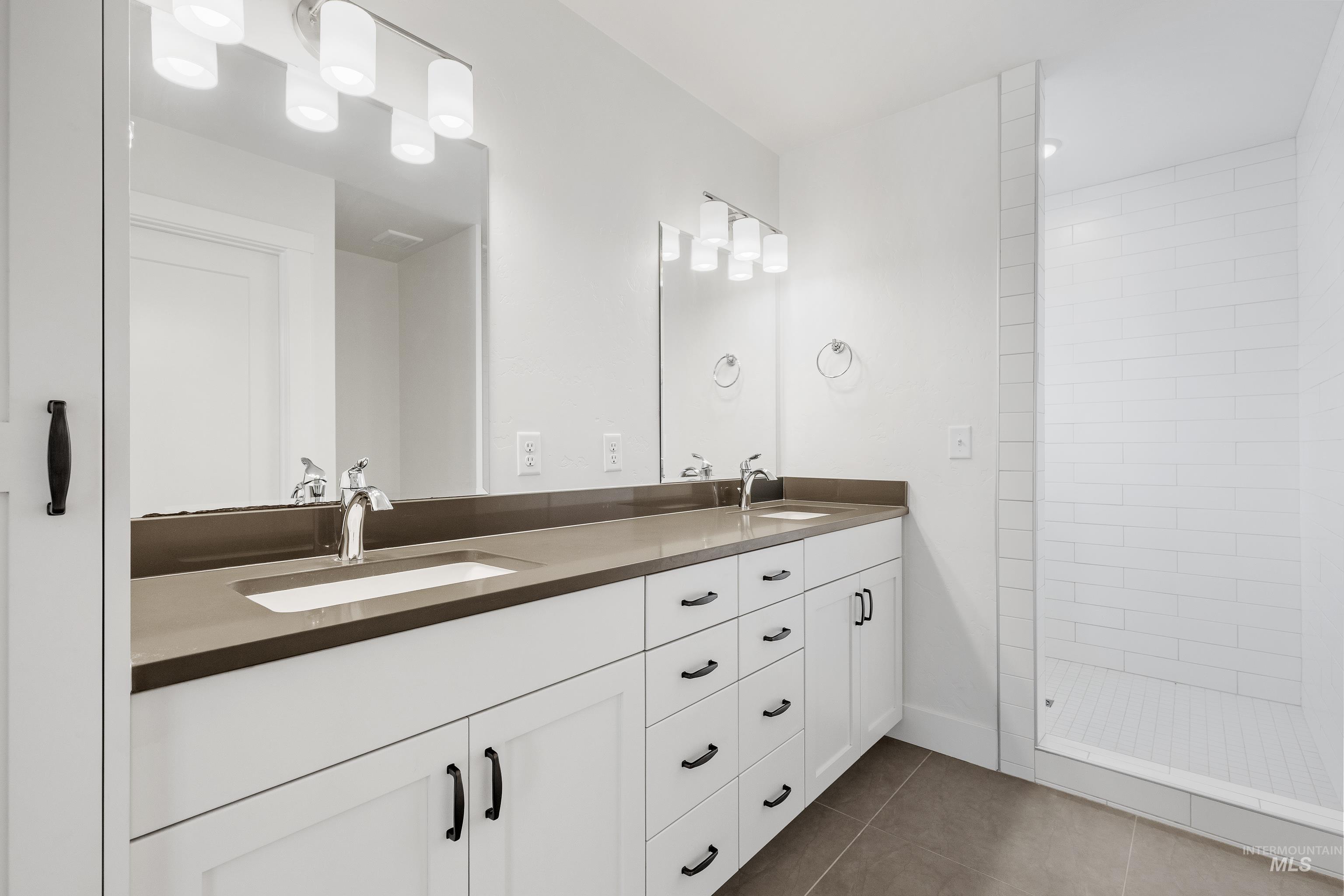 Full bath with dark tile patterned flooring, double vanity, and a stall shower
