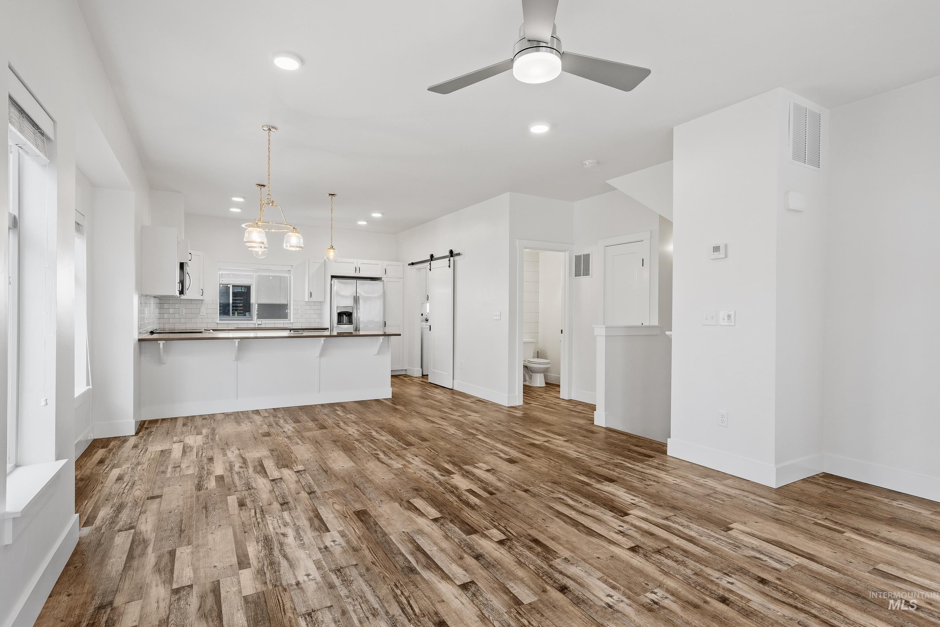 Unfurnished living room featuring a barn door, recessed lighting, light wood-type flooring, and a ceiling fan