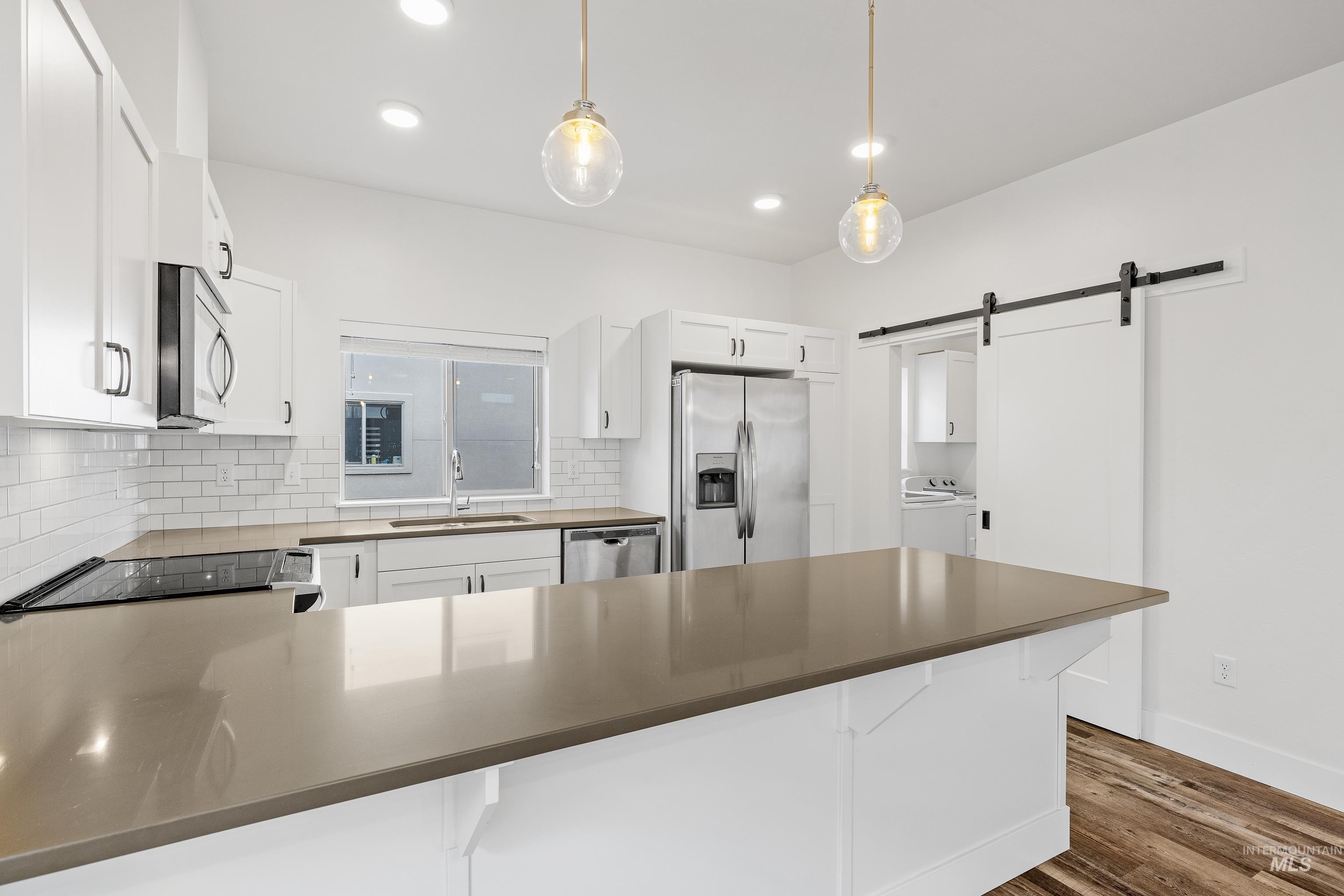Kitchen featuring a barn door, decorative light fixtures, white cabinets, decorative backsplash, and a peninsula