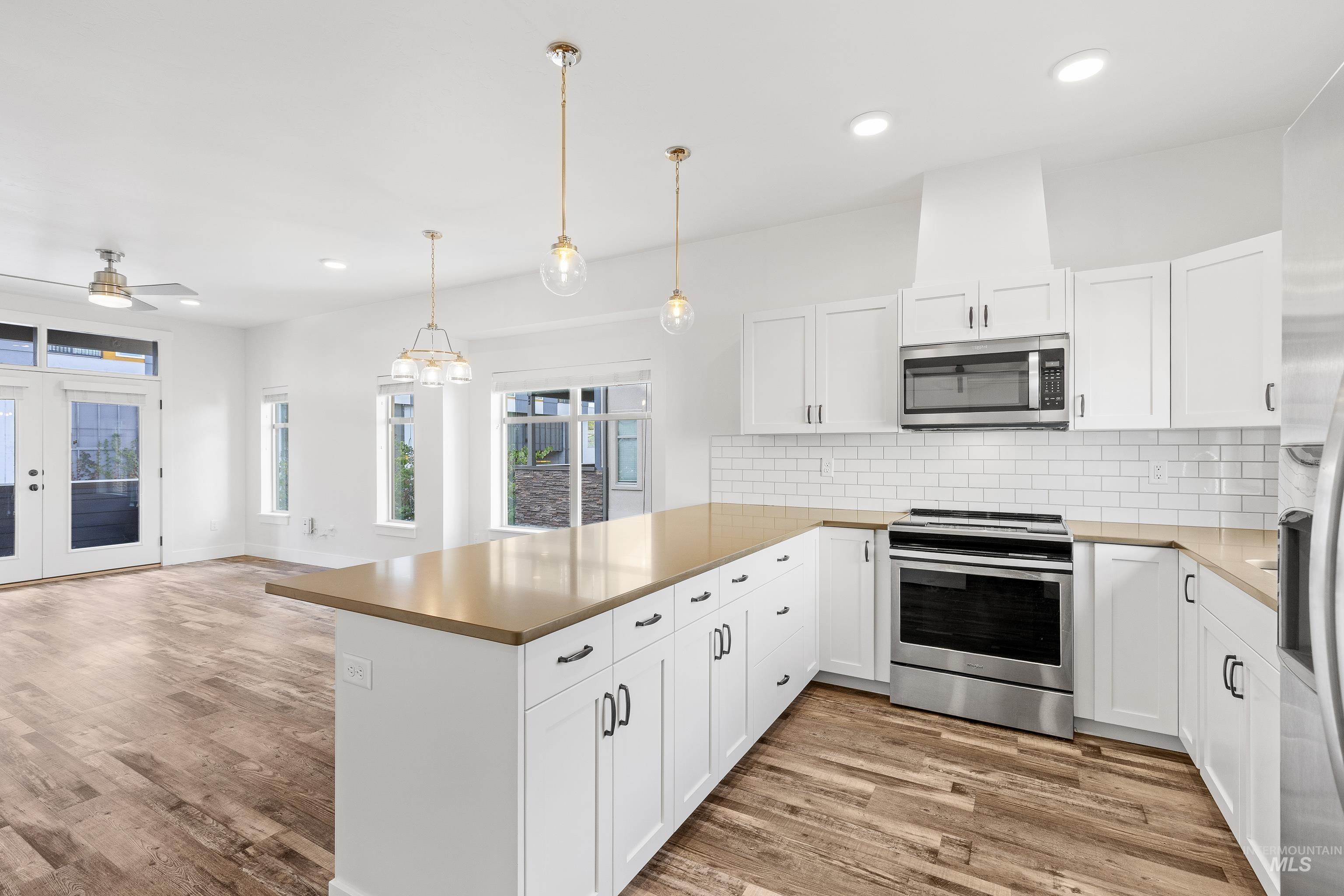 Kitchen featuring appliances with stainless steel finishes, a peninsula, white cabinets, backsplash, and light wood-style flooring