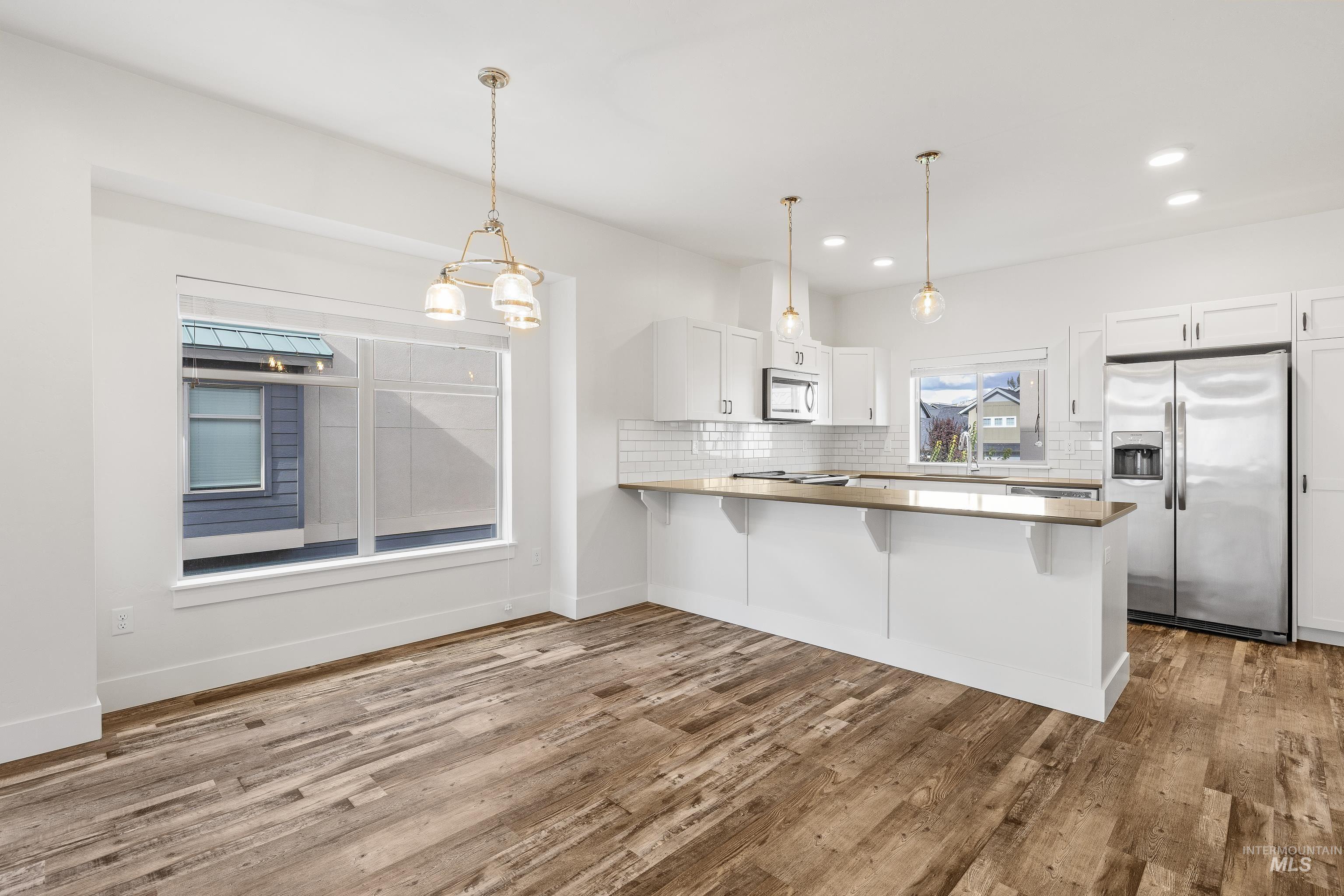 Kitchen with white cabinetry, hanging light fixtures, stainless steel appliances, decorative backsplash, and light countertops