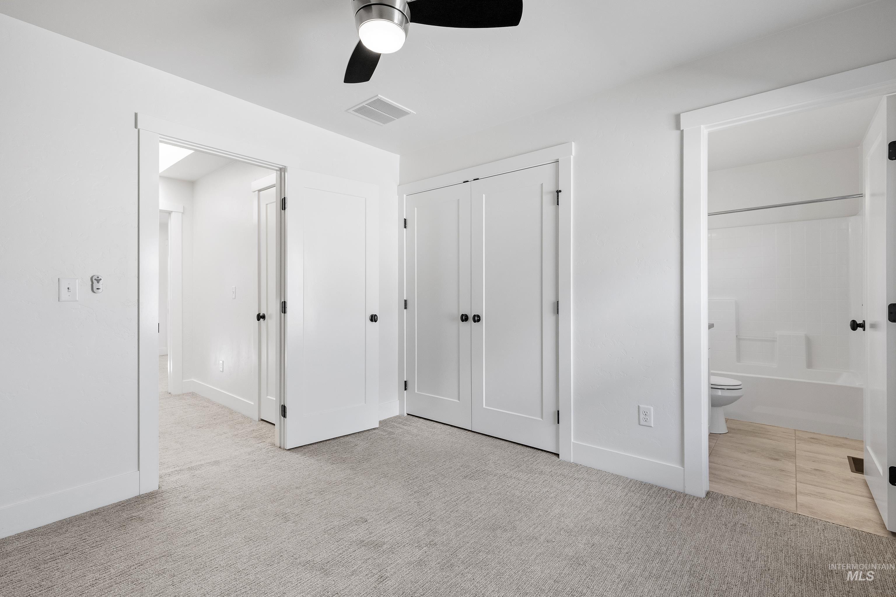 Unfurnished bedroom featuring light colored carpet, a ceiling fan, connected bathroom, and a closet