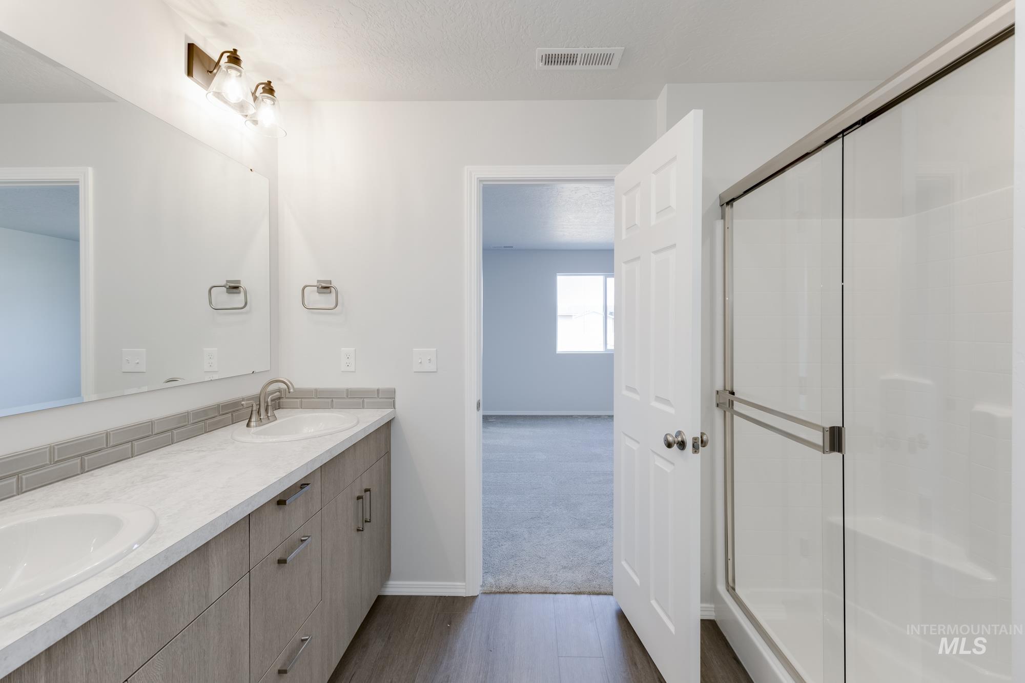 Full bathroom featuring double vanity, dark wood-style floors, a shower stall, a textured ceiling, and dark carpet