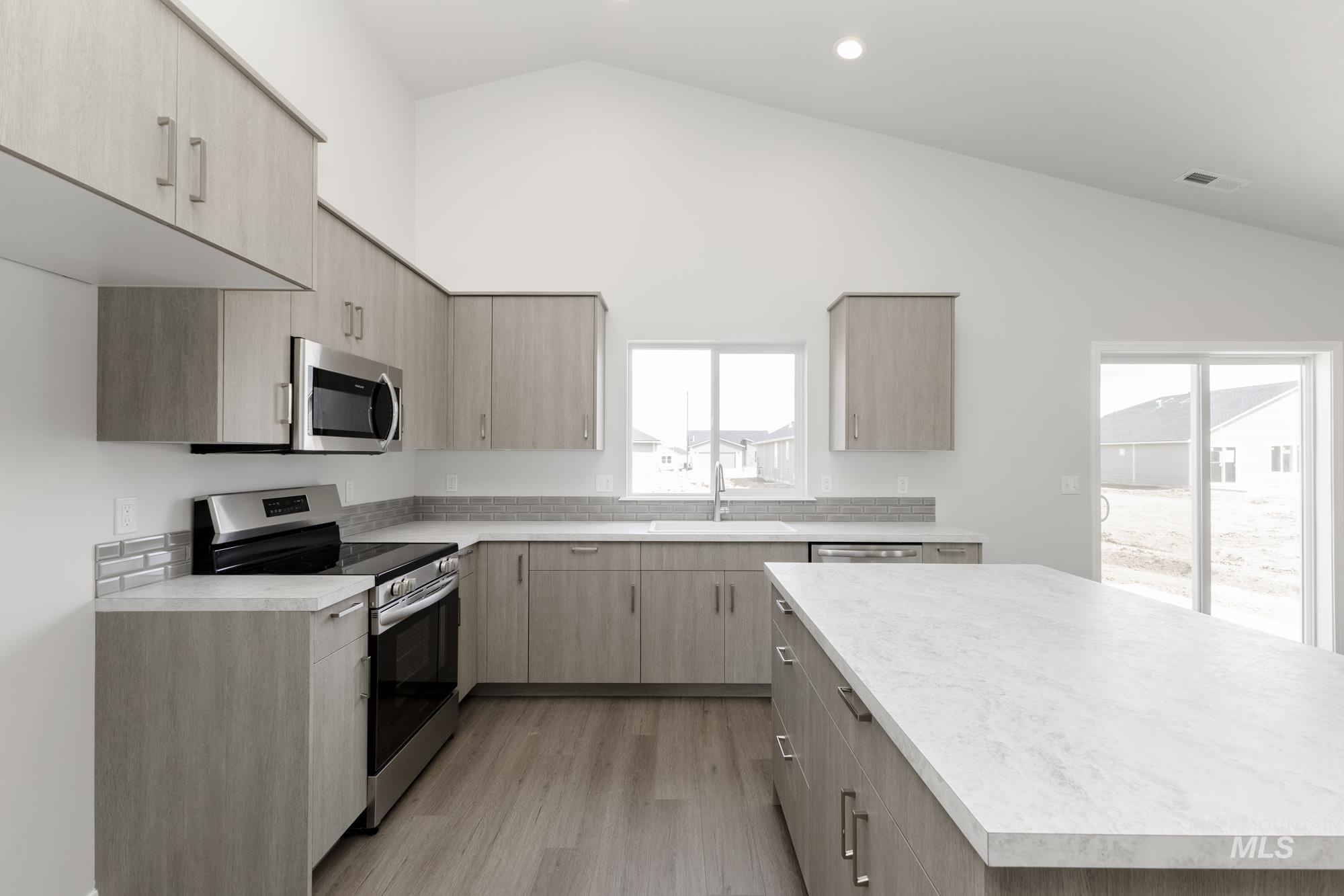 Kitchen with light brown cabinets, stainless steel appliances, light countertops, recessed lighting, and high vaulted ceiling