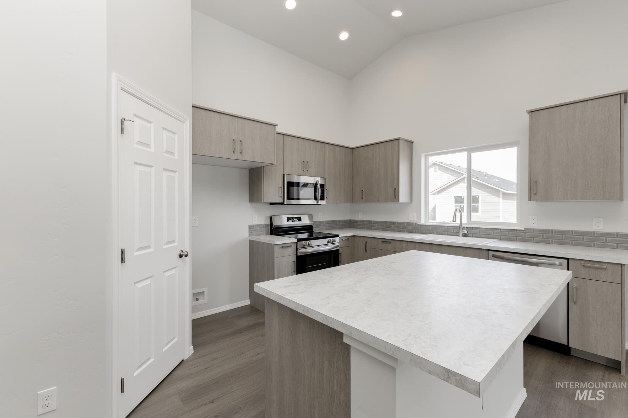 Kitchen featuring light countertops, appliances with stainless steel finishes, light brown cabinetry, a center island, and modern cabinets