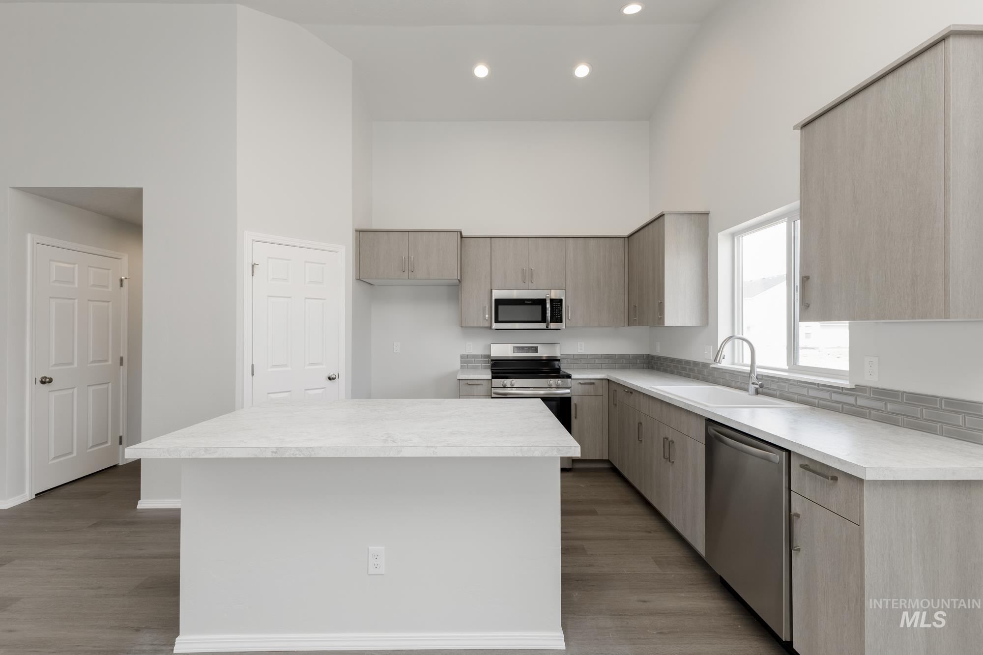 Kitchen featuring a towering ceiling, light countertops, appliances with stainless steel finishes, modern cabinets, and recessed lighting
