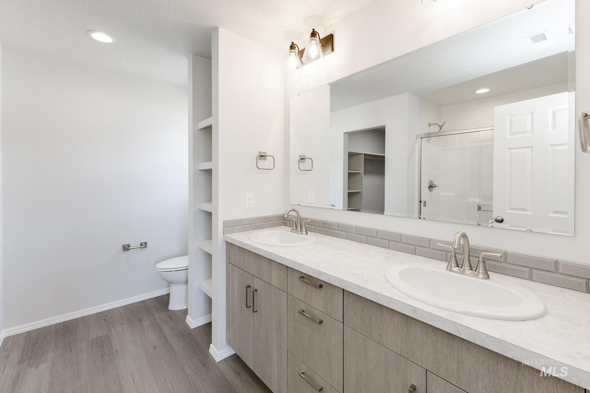 Full bath featuring a stall shower, double vanity, light wood-style floors, recessed lighting, and a spacious closet